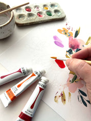 Artistic scene with MEEDEN paint tubes, a brush, and a floral painting on paper.