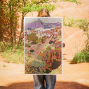 Person holding a colorful landscape illustration in front of a natural rock formation.